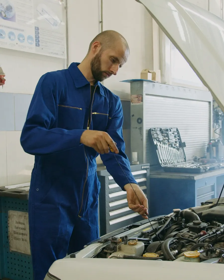 Un mécanicien contrôle le niveau d'huile d'un moteur, capot ouvert, avant toute intervention